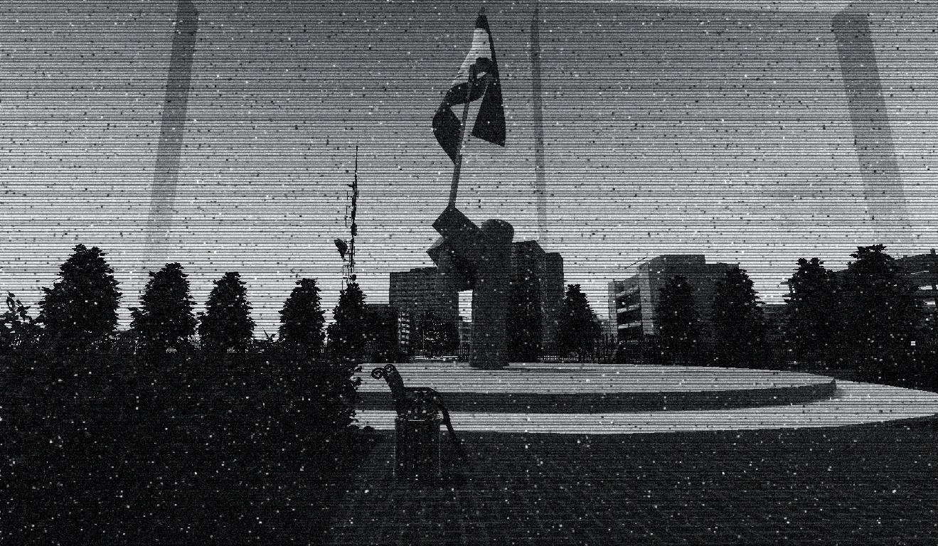 A plaza with a flag monument, trees and apartment blocks in the background