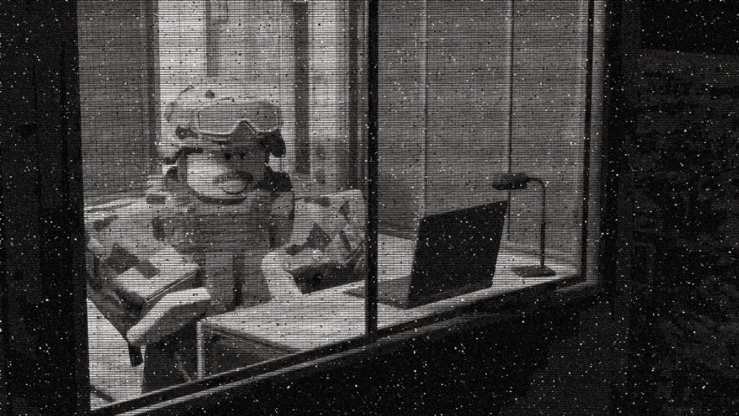 A soldier in a helmet and goggles seated at a desk with a laptop, seen through a window grid